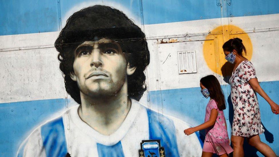 A woman and a girl walk by a mural of Diego Maradona on November 27, 2020 in Avellaneda, Buenos Aires Province, Argentina.