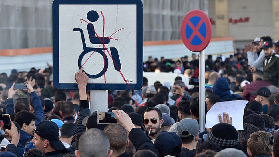 Algerian demonstrators hold a placard with the symbol of a man on a wheelchair