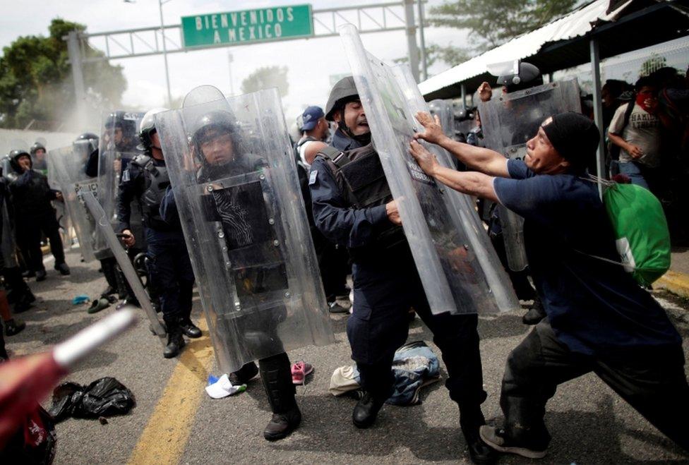 A Honduran man hits the shield of a riot policeman after storming the Guatemalan checkpoint to enter Mexico