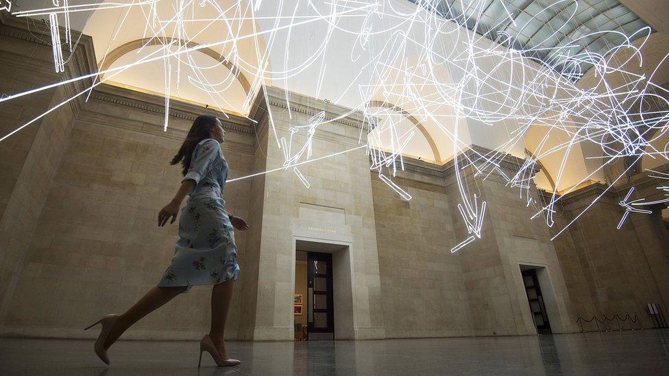 A gallery assistant walks under the neon sculpture