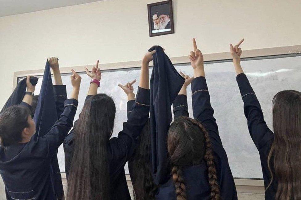 Iranian schoolgirls without headscarves raise their middle fingers towards portraits of Ayatollah Ruhollah Khomeini and Ayatollah Ali Khamenei