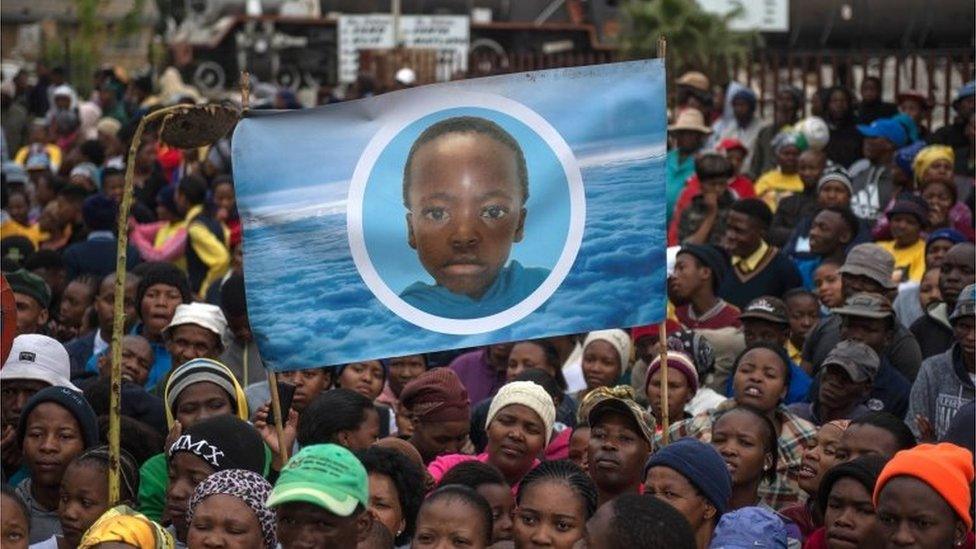 Residents from the Scotland informal settlement in Coligny hold a portrait of late 16-year-old Moswi Matlhomala Moshoeu during a protest outside the Coligny Magistrate court on May 8, 2017