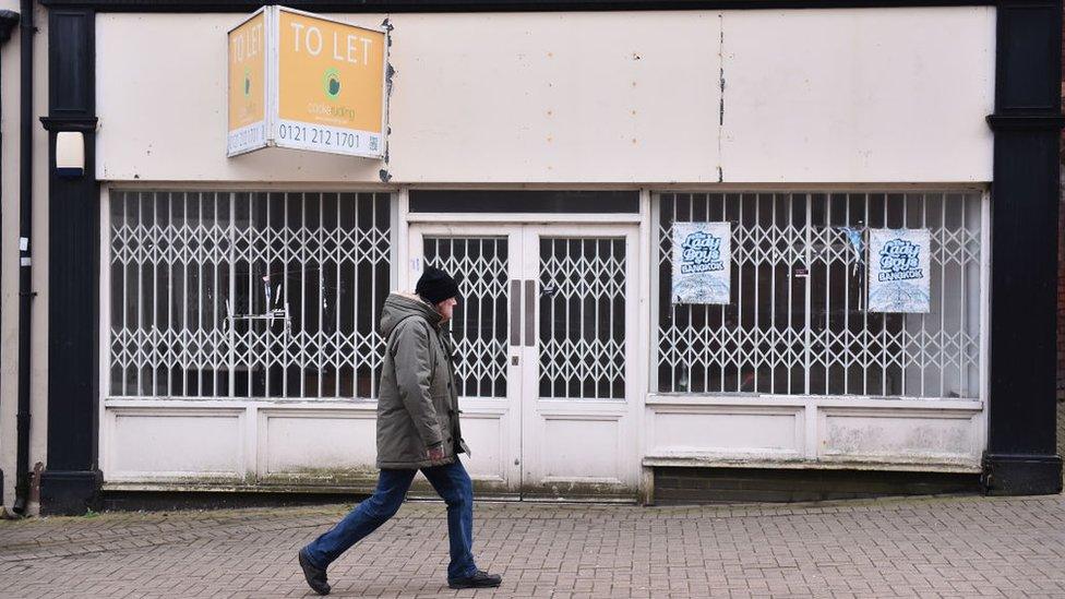 Man walking past a boarded up sho[