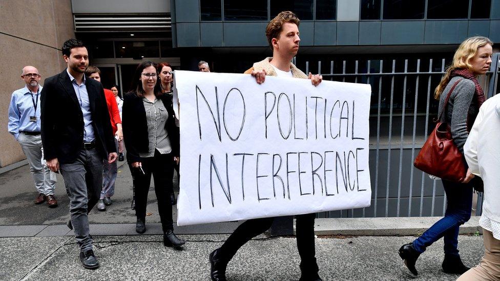 Journalists walk of the ABC in Sydney, with one carrying a 'No political interference' sign