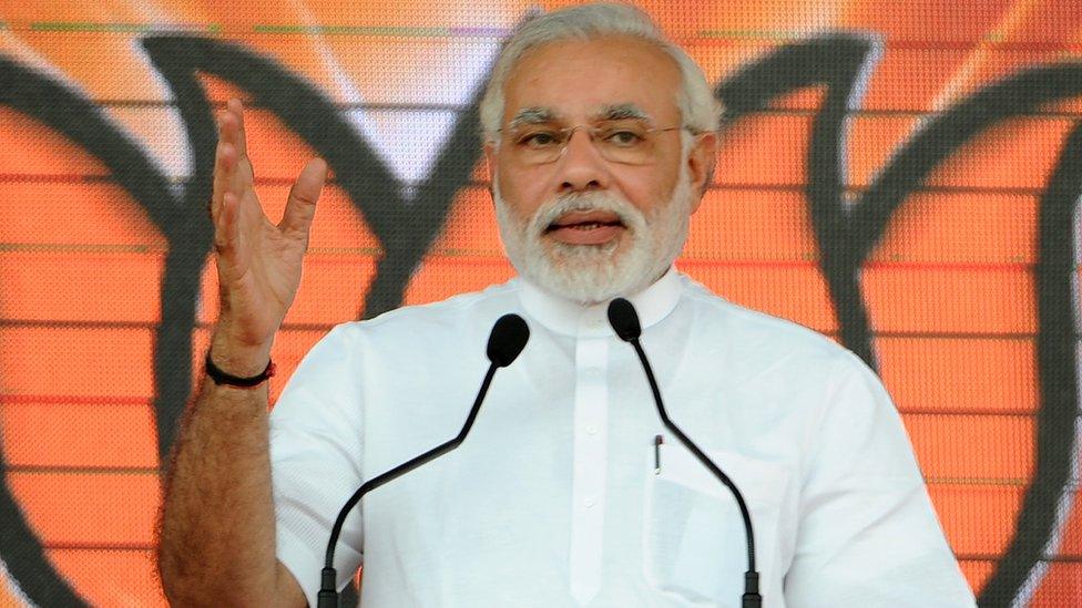 Narendra Modi wearing white in front of an orange background addresses a rally.