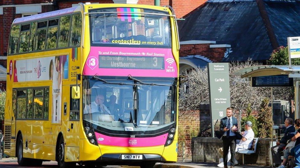 Yellow double-decker bus next to a bus stop with people waiting