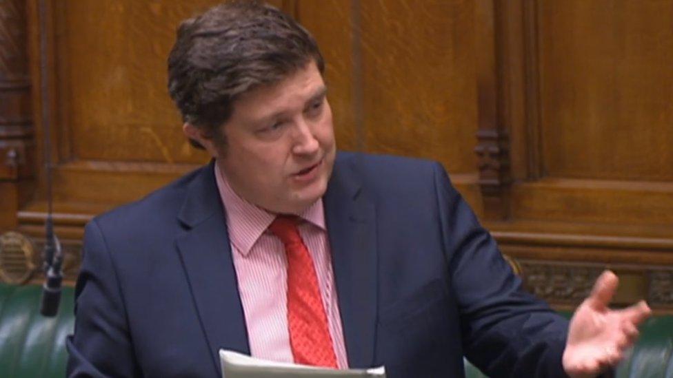 Andrew Lewer wearing a blue jacket and red tie speaking in the House of Commons