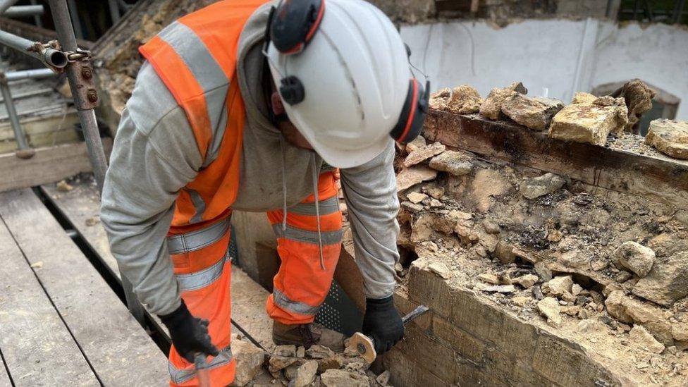 A workman dismantling brickwork