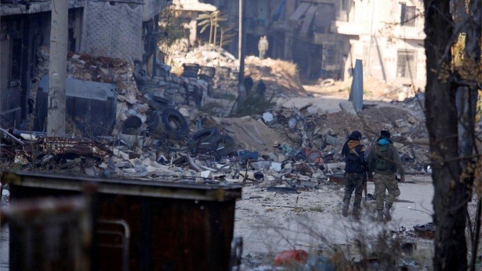 Forces loyal to Syria's President Bashar al-Assad walk past damaged buildings in a government held area of Aleppo, Syria on 9 December 2016.