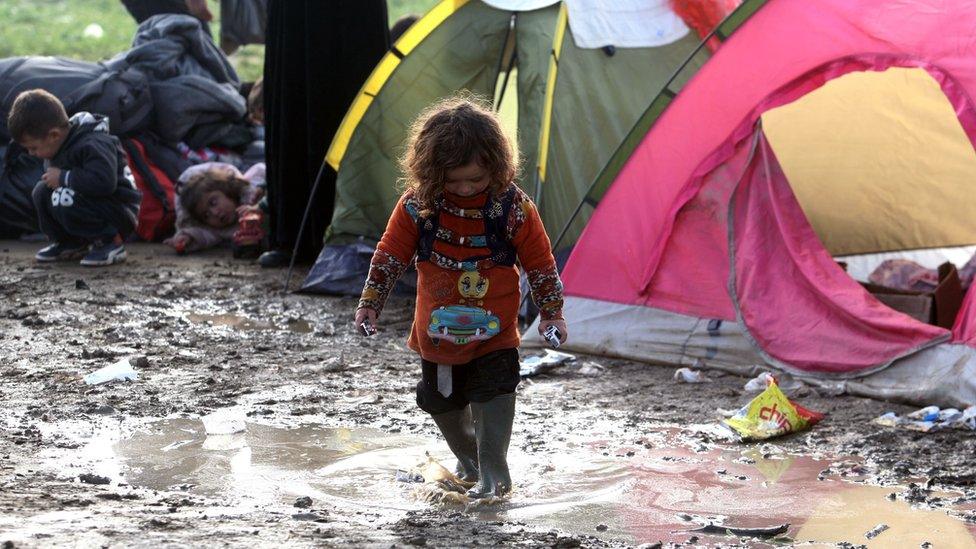 A girl plays in the mud in a tent camp near the village of Idomeni, on 1 March, 2016 as migrants and refugees walk to cross the Greece-Macedonia border.