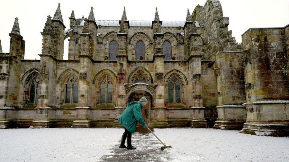 A woman clears a light dusting of snow outside Rosslyn Chapel in Midlothian