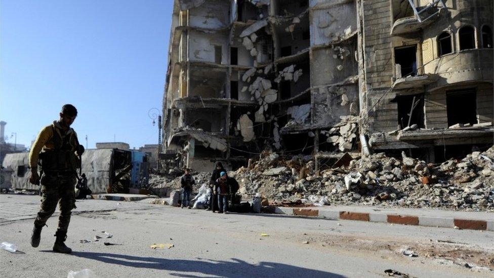 A member of Forces loyal to Syria's President Bashar al-Assad carries his weapon as he walks past damaged buildings in a government held area of Aleppo, Syria on 9 December 2016.