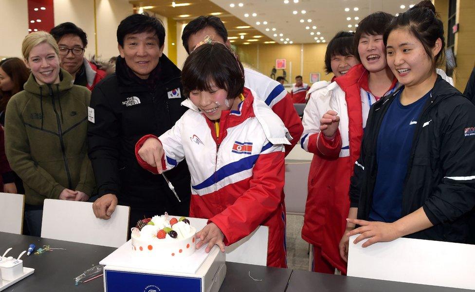 North Korean female ice hockey player Choe Un Gyong (C) cutting a cake while her North and South Korean teammates celebrate