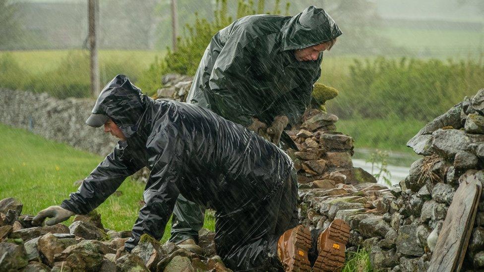 Two men repairing a drystone wall in the Yorkshire Dales in the rain