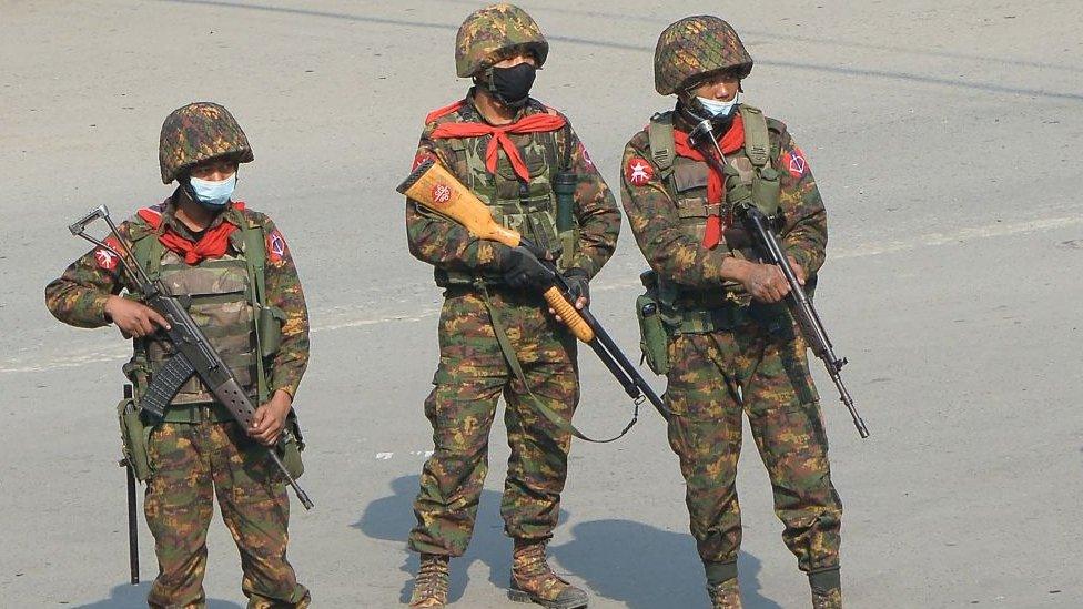 Soldiers carrying firearms look on as protesters hold a demonstration against the military coup