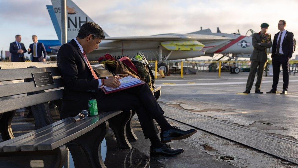 A photo from Rishi Sunak's social media showing the PM reading his notes on the tarmac of an airfield, with fighter jets in the background