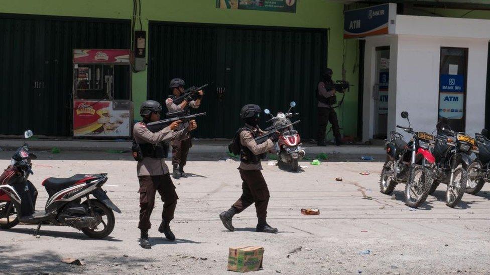 Police fire warning shots outside a shop in Palu, Indonesia