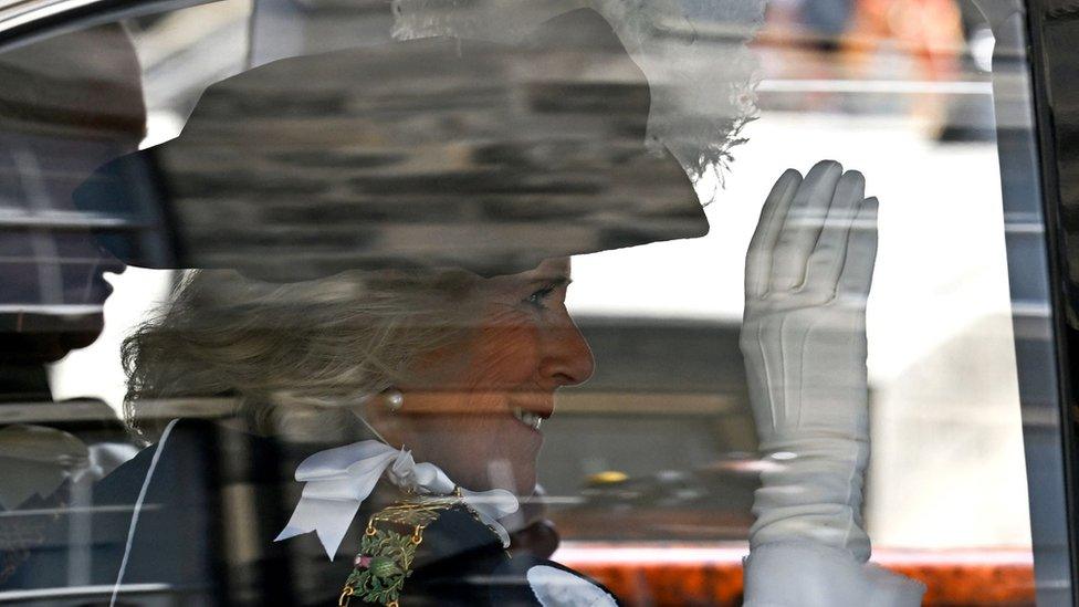 Close up of Queen Camilla through car window, wearing a white glove and waving