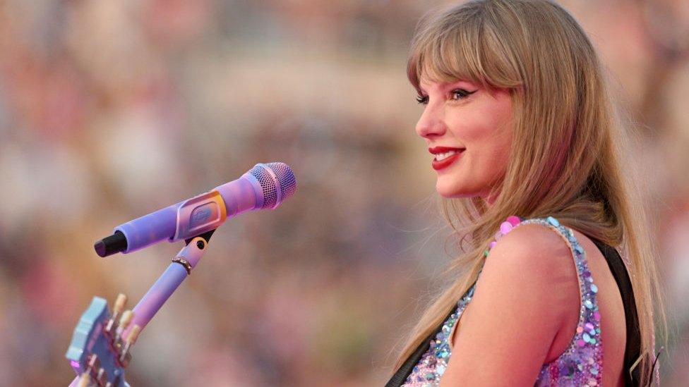 Taylor Swift on stage, her side profile is facing the camera and she's smiling