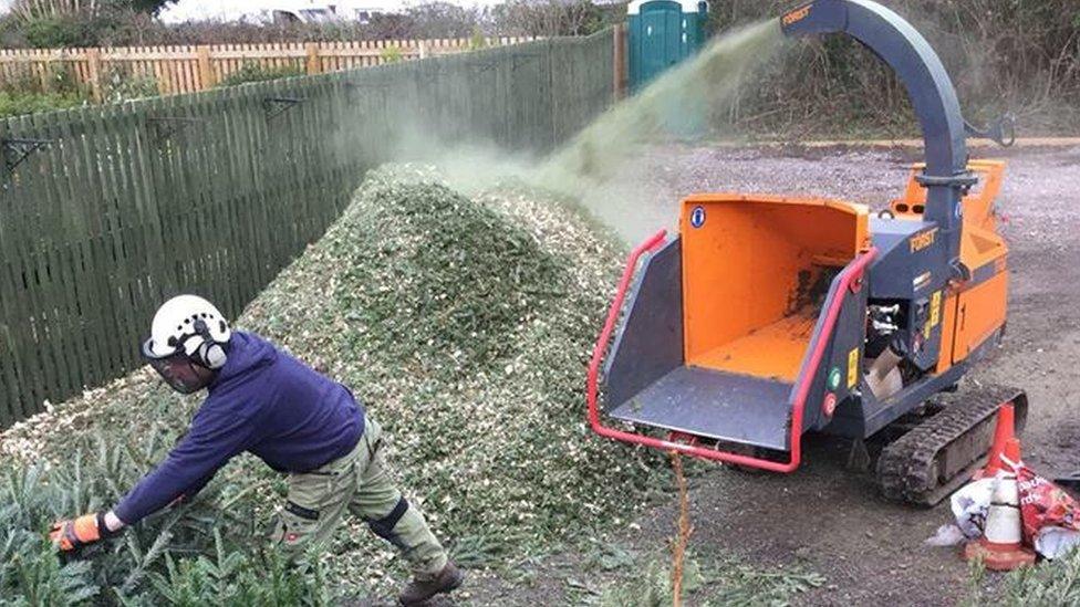 Man wearing protective gear next to a bright orange chipper and a big pile of chippings