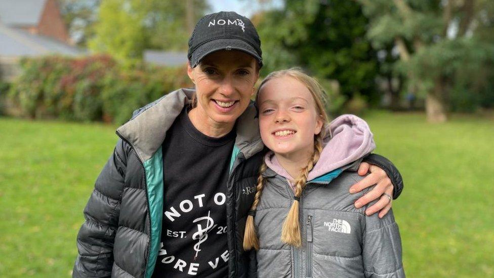 Woman in blue cap and girl in grey jacket with pigtails.