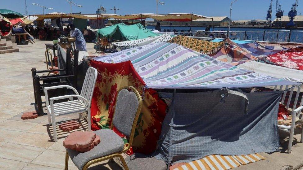 Sudanese families and people from Syria and Yemen nationalities protect themselves from the heat of the sun as they wait with their luggage at a camp center next to the port to be processed for evacuation, following the crisis in Sudan's capital Khartoum, in Port Sudan, Sudan, May 4