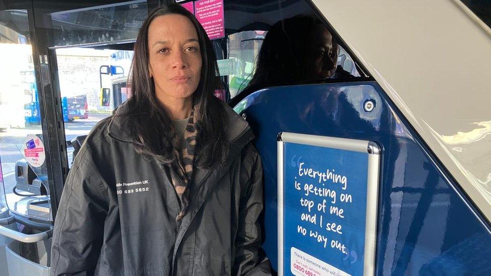 Marianne Ramnath standing by a poster on a bus that says "Everything is getting on top of me and I see no way out"