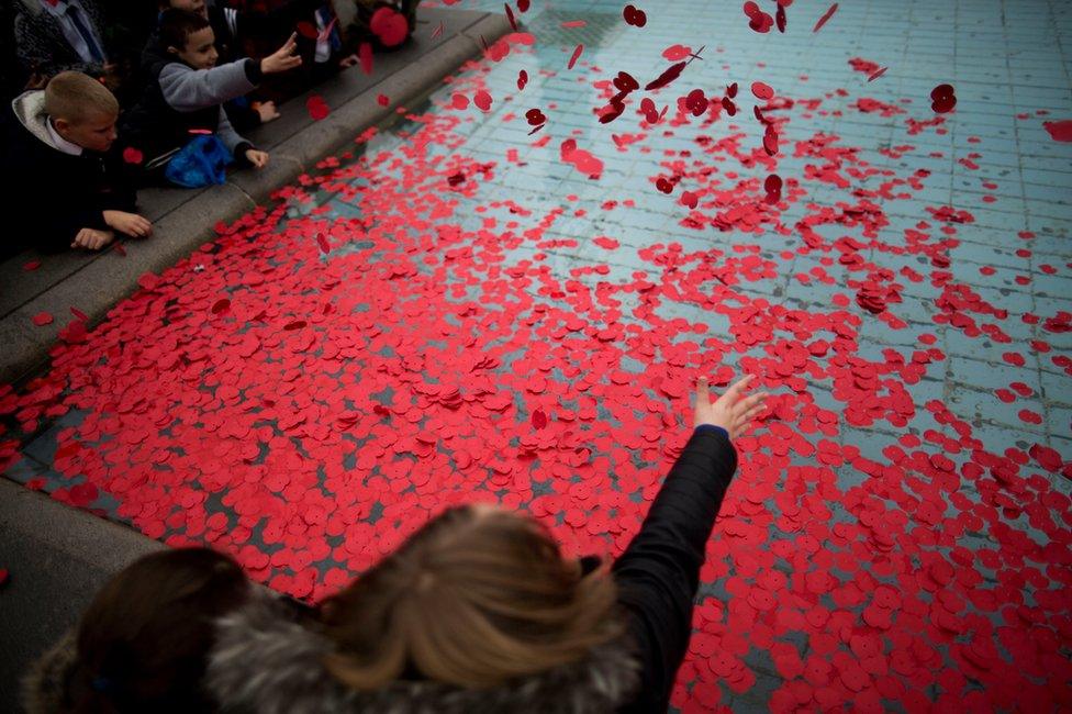 People throw poppies into a fountain in Trafalgar Square, London