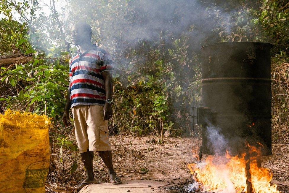 Kumus Da Silva (fight), inspects the fire cooking of cashews near his home just outside the capital. Da Silva supports his family with the cashews and cashew juice he sells domestically.