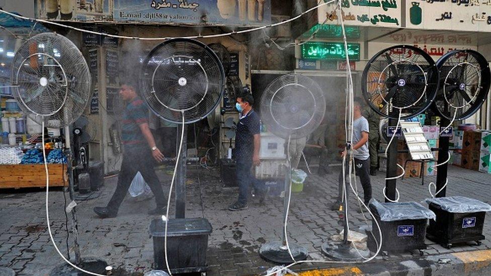 People walk past fans spraying air mixed with water vapour deployed by donors to cool down pedestrians