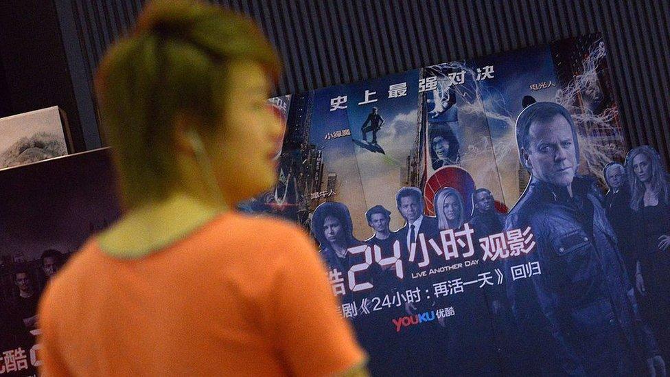 Man walks past a cinema poster where Chinese video-sharing website Youku Tudou, was holding a 24-hour event for the release of the new season of US television show '24' in Beijing