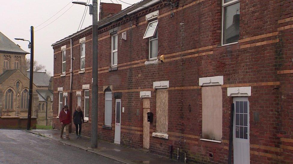 Mr Fallow walking along a street of boarded-up houses