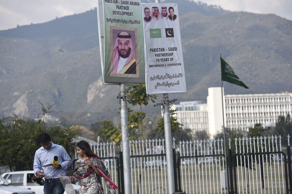 Reporters walk under a sign saying "Pakistan-Saudi Arabia partner development" and a picture of Mohammad Bin Salman