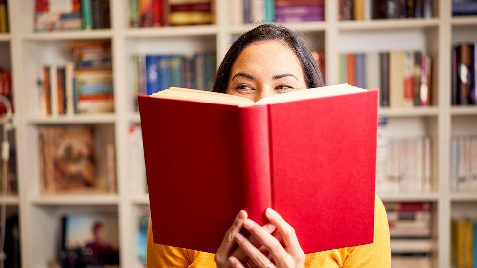 File photo of a woman reading a book in front of a bookcase