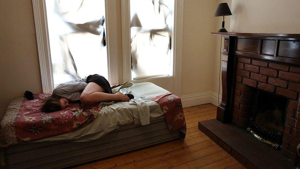 A woman sheltering on a bed looking scared