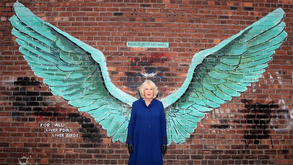 The Duchess of Cornwall stands between the wings of artist Paul Curtis' mural entitled For All Liverpool's Liver Birds