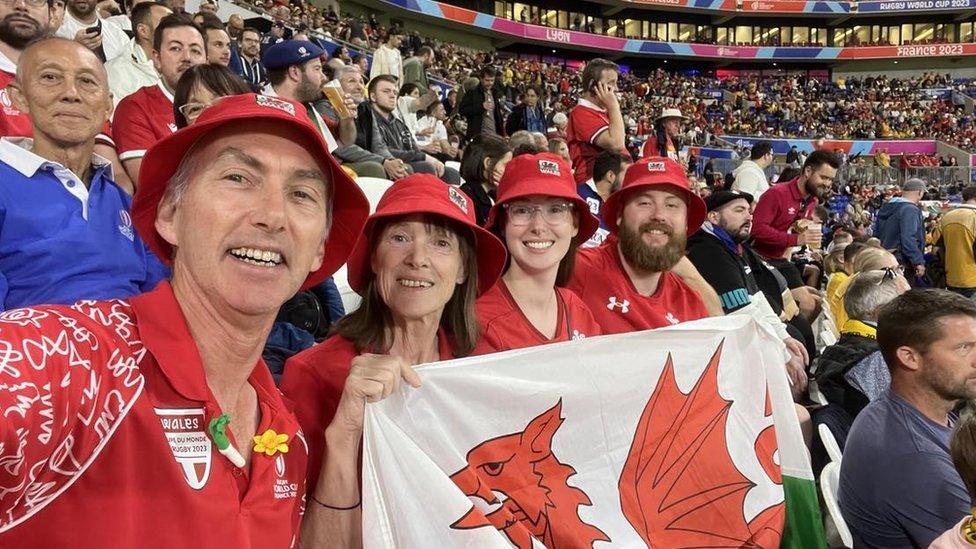 Nigel Dumont-Jones in a red Wales jersey and hat in a stadium of rugby fans