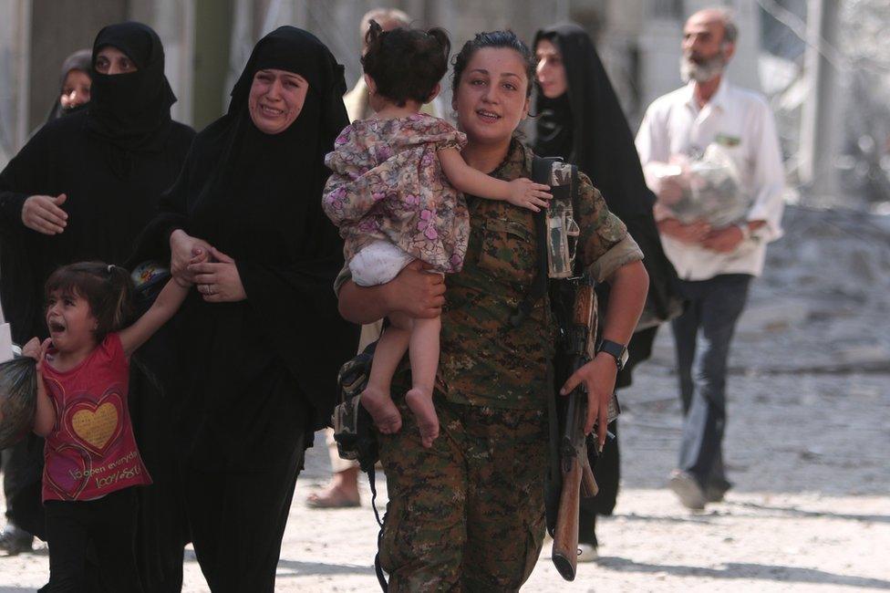 A fighter helps civilians who were evacuated an Islamic State-controlled neighbourhood of Manbij, Syria, 12 August