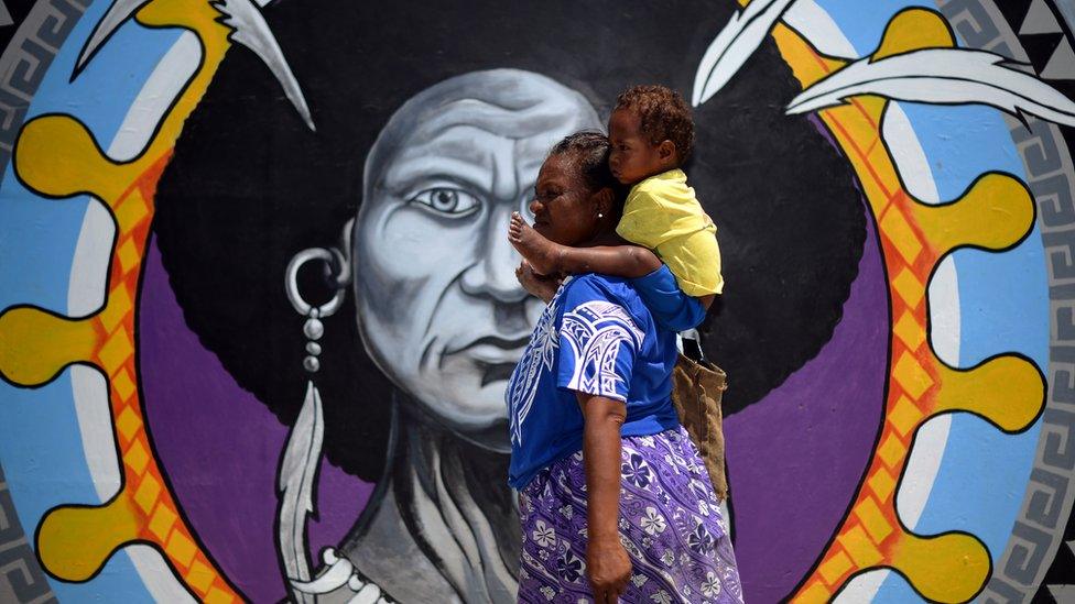 A Papuan woman walks in front of a mural in downtown Port Moresby on November 13, 2018, ahead of the Asia-Pacific Economic Cooperation (APEC) summit in Port