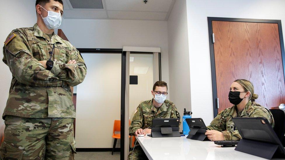 US national guard members are being trained for task in Tumwater, Washington - one person standing in a room and two sitting, all wearing masks