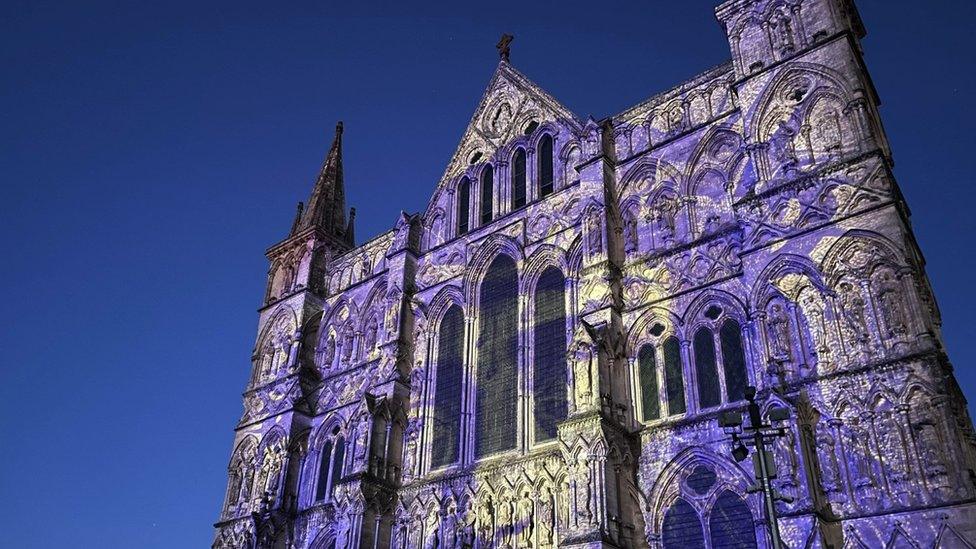 Image of the Sarum Lights exhibition at Salisbury Cathedral. The building has blue and yellow patterns projected onto it.