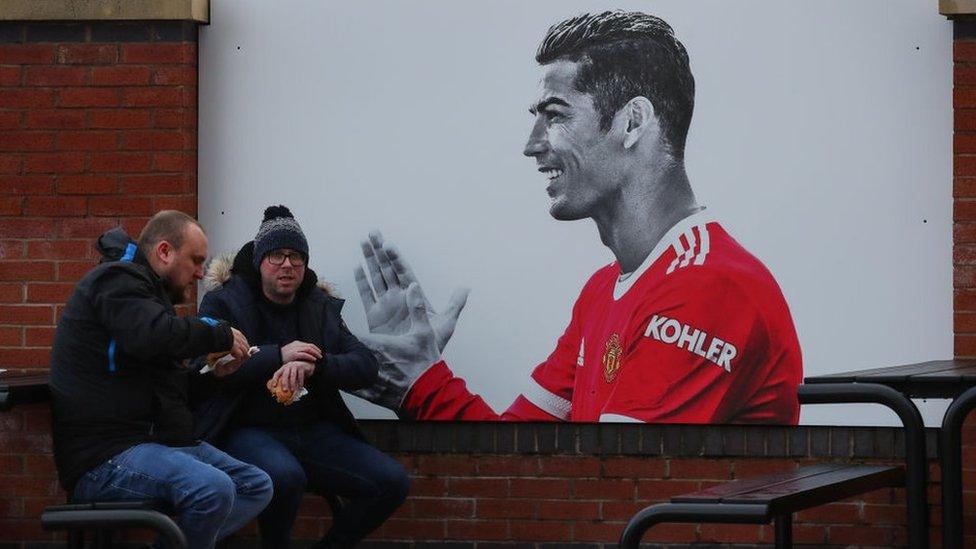 Fans sit next to a mural of Cristiano Ronaldo of Manchester United ahead of the Premier League match between Manchester United and Crystal Palace at Old Trafford on December 5, 2021 in Manchester, England.