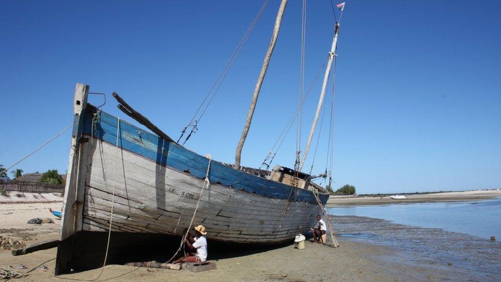 Two men kneel down to repair the hull on their sailing boat