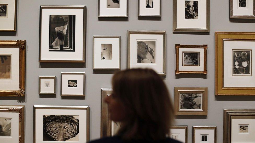 Woman stands in front of a group of photographs at the exhibition