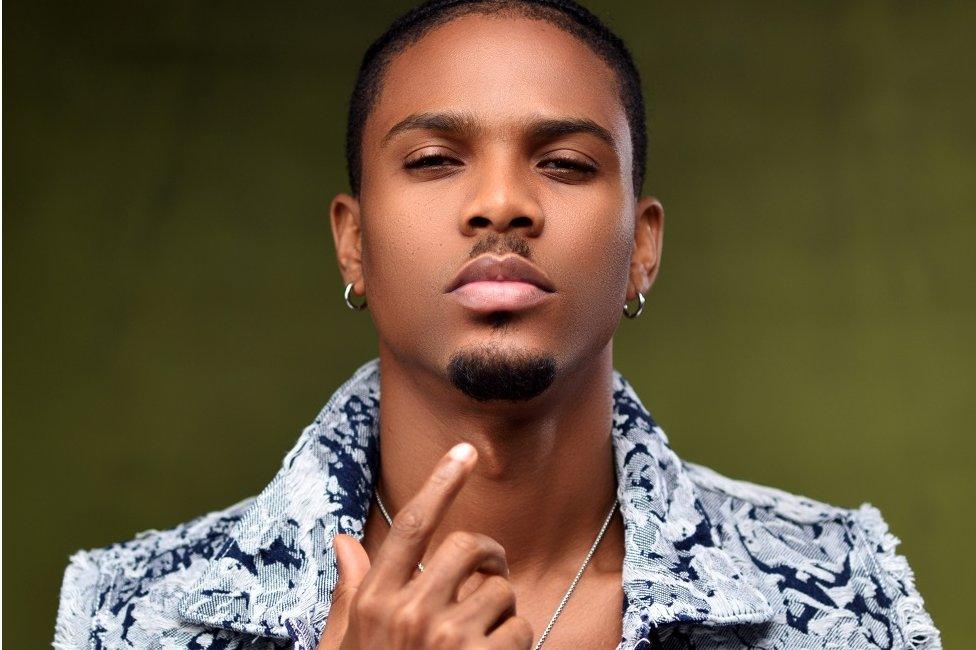 JZyNO posing in a studio. He is wearing a light blue jacket which is unbuttoned.