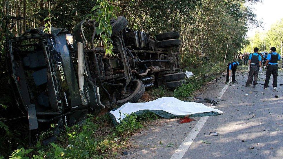 Thai bomb officers squad inspect a damaged military patrol vehicle lying in a ditch near a pool of blood on the road (C) in Yala province on February 10, 2013 following a bomb attack by suspected insurgents.