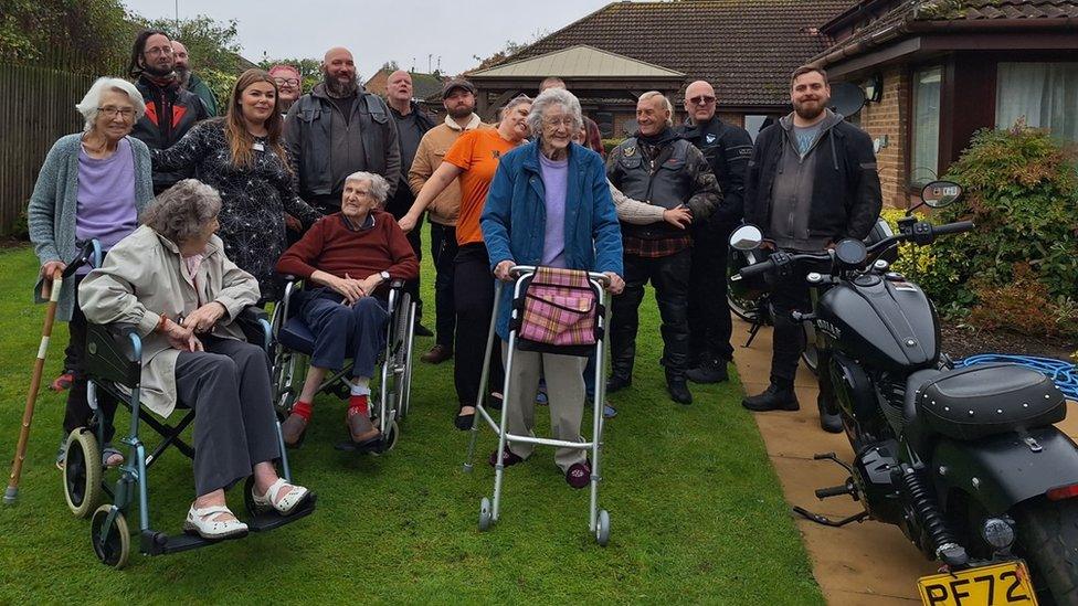 Women, some using wheelchairs and walking frames, crowd round one of the bikes