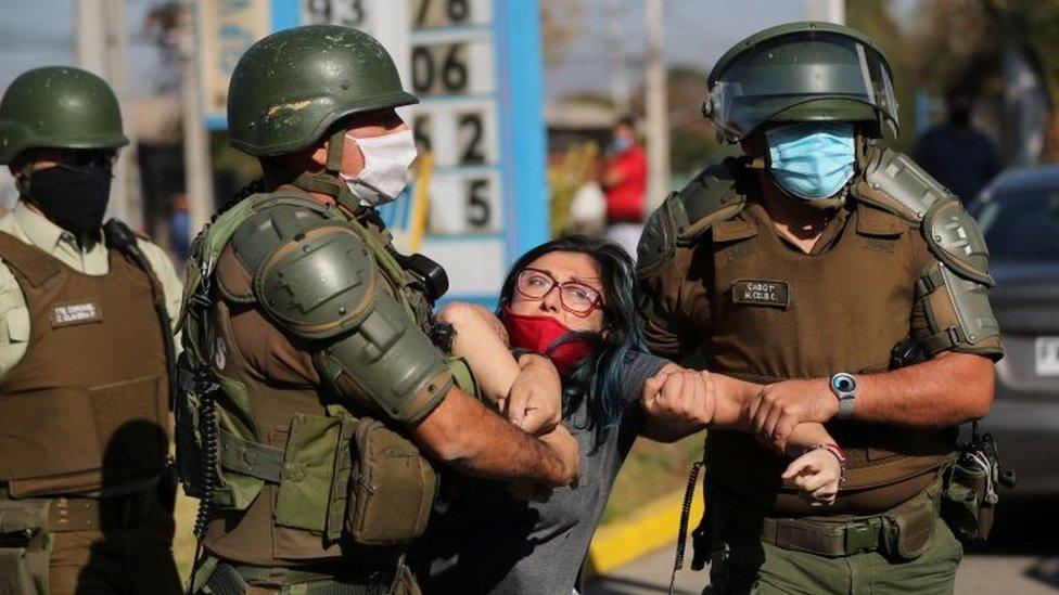 A woman is detained after shouting slogans against riot police at a poor neighbourhood where people are protesting about the lack of help from the government,