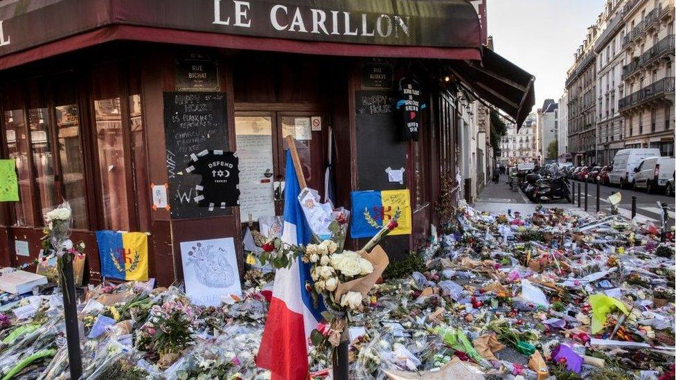 Flowers, candles and flags laid in tribute to people killed in the attack on Le Carillon bar in Paris.