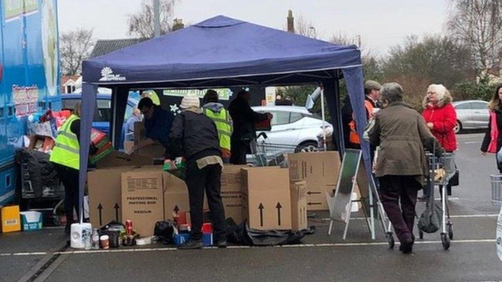 People donating items for Ukraine under a gazebo in Morrison's car park in Dereham, with a lorry being loaded with boxes